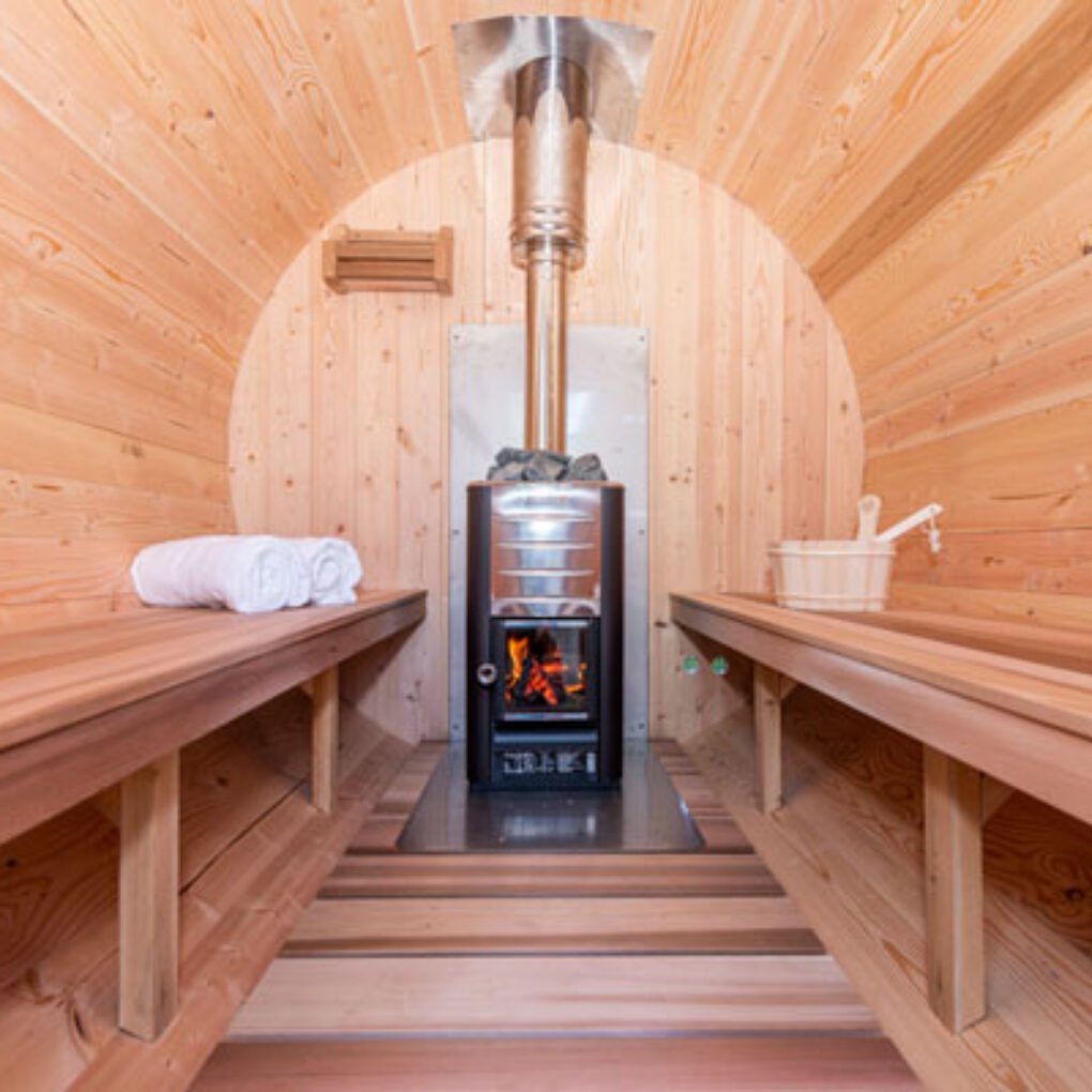 Interior of a Leisurecraft Backyard Barrel Sauna for Sale with wooden benches and a wood-burning stove