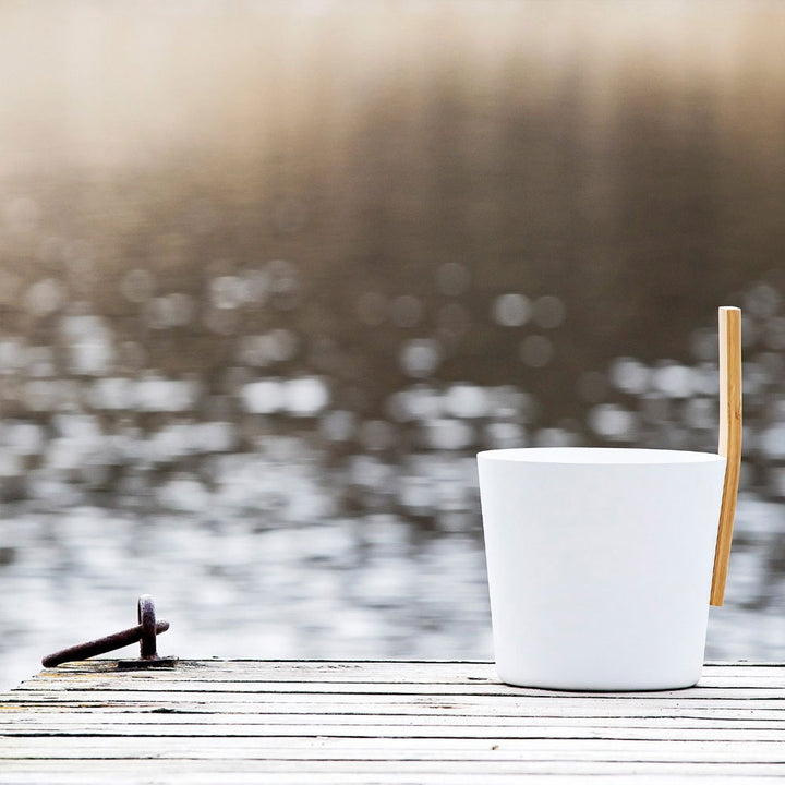 White KOLO sauna accessories bucket with wooden handle placed on a dock by the water
