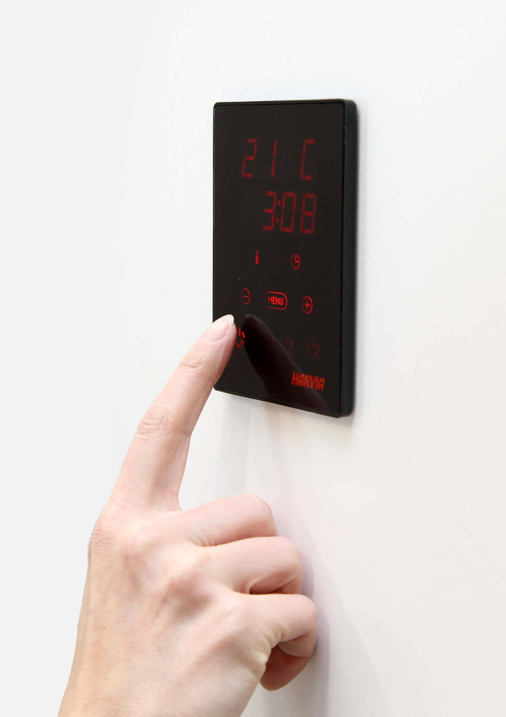 Hand adjusting Harvia CX30C-U1 control package black digital sauna control panel on white wall