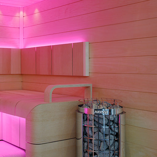 Harvia Cilindro PC80E electric sauna heater with stone basket beside light wood benches and pink LED lighting