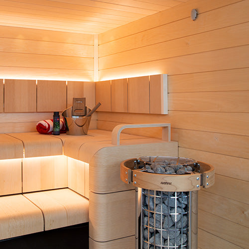 Harvia Cilindro PC90 sauna heater beside light wood sauna benches with bucket and stones