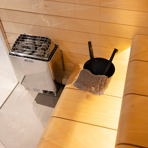 Harvia KIP30B electric sauna heater installed in a wood paneled sauna corner with bench bucket and ladles
