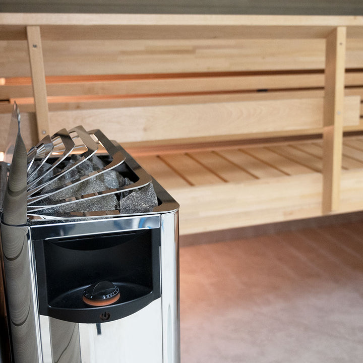 Harvia The Wall electric sauna heater stainless steel with stones next to wooden bench