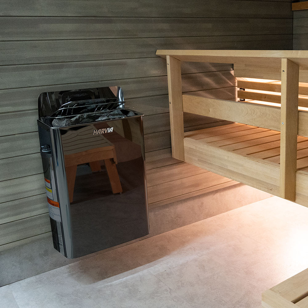 Harvia The Wall sauna heater mounted on sauna wall next to wooden bench with sauna stones
