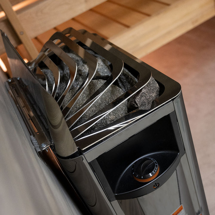 Harvia wall-mounted electric sauna heater with black steel casing and sauna stones by wooden bench