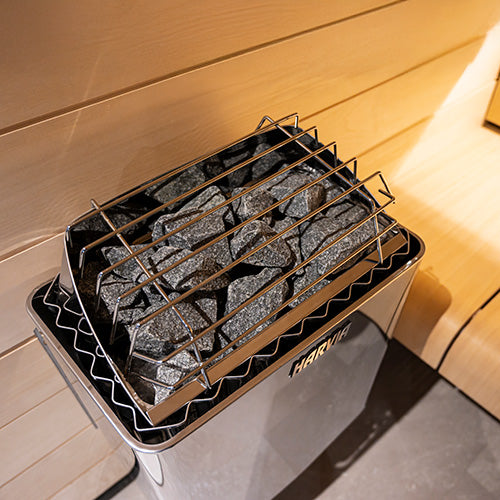 Harvia wall-mounted electric sauna heater with stones in a wooden sauna interior