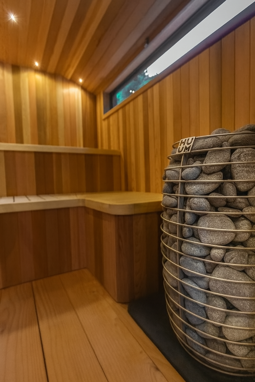 HUUM HIVE Mini Series sauna heater with stones inside a wooden sauna room with bench and window
