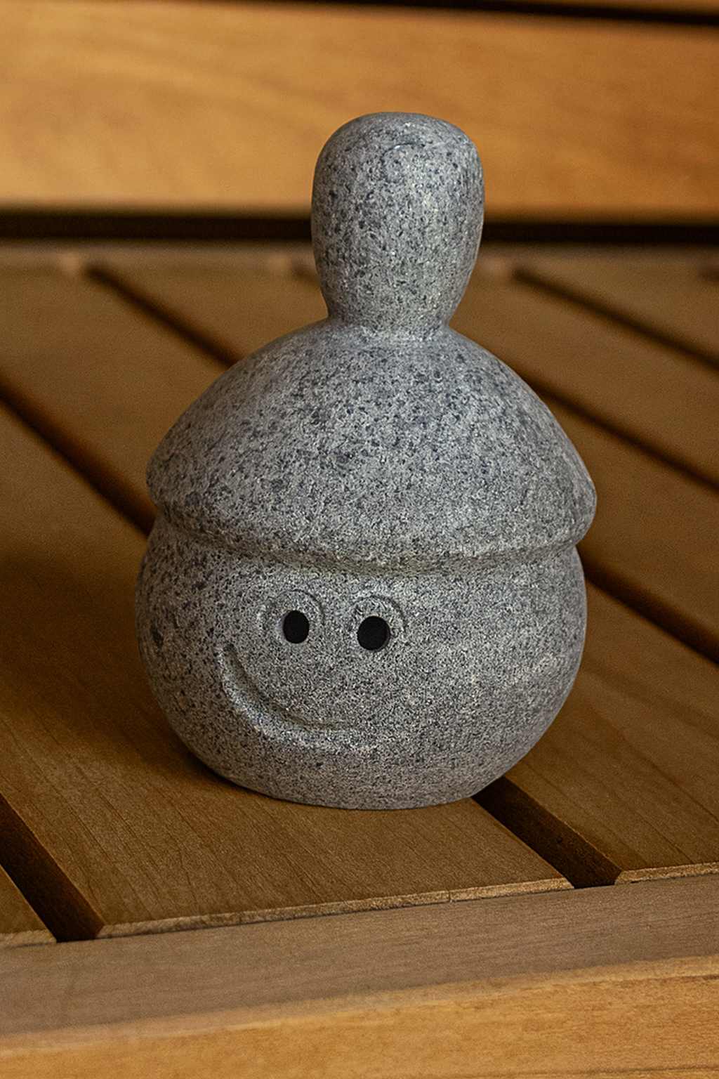 Hukka Elli sauna stone figurine gray smiling stone accessory on wooden sauna bench decorative sauna ornament