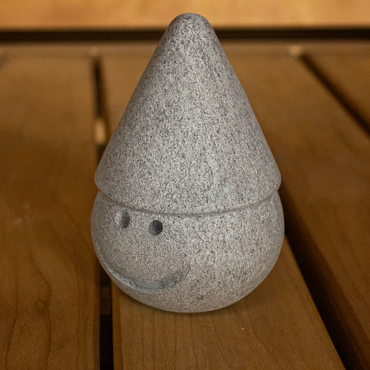 Hukka Tahvo Sauna Elf gray stone sauna accessory with smiling face and conical hat on wooden bench