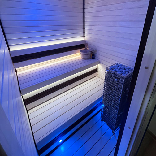 HUUM CLIFF 11kW electric sauna heater in modern sauna room with white wooden benches and blue lighting