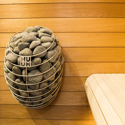 HUUM DROP 6kW sauna heater mounted on wooden wall filled with sauna stones next to wooden bench