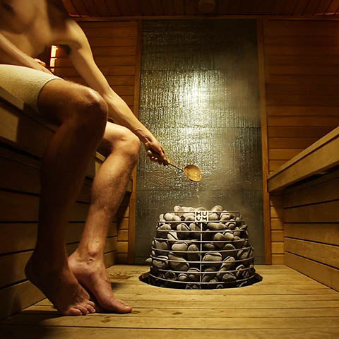HUUM HIVE electric sauna heater with sauna stones in wooden sauna room with person pouring water