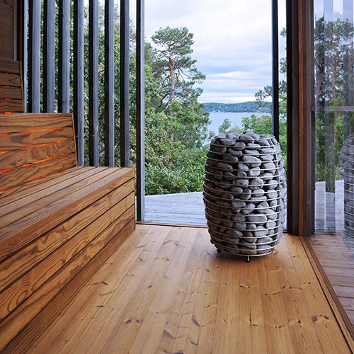HUUM HIVE electric sauna heater with stacked stones in wooden sauna room overlooking nature