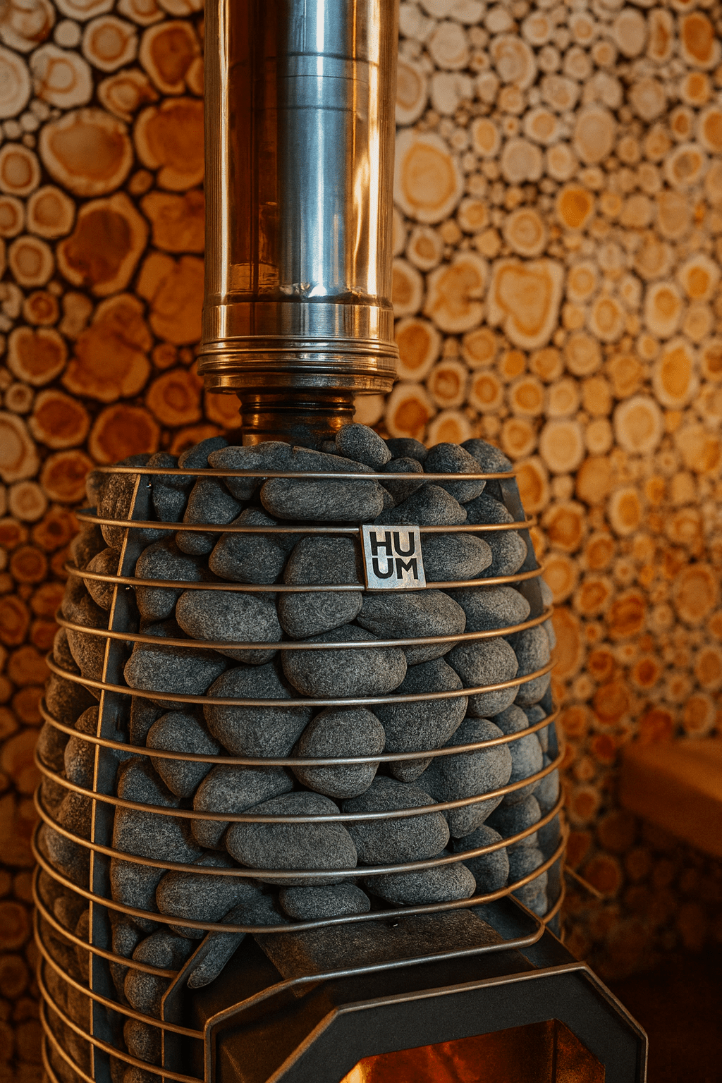 HUUM HIVE Flow Mini sauna heater with stacked stones and a polished metal chimney for relaxing sauna experiences