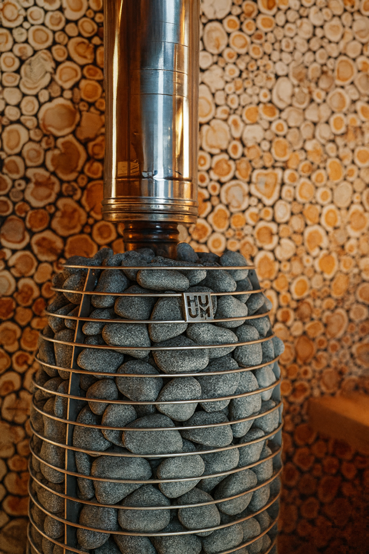 HUUM HIVE Flow Series sauna heater with stacked stones and metal casing in wooden sauna interior