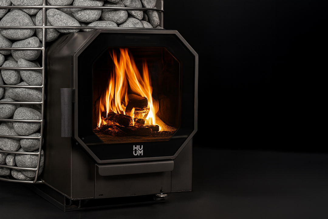 HUUM HIVE Flow Series sauna heater with visible flames and stacked sauna stones on black background