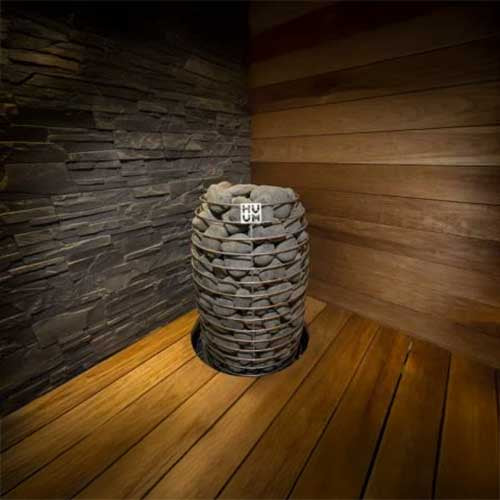 HUUM HIVE Mini 9kW electric sauna heater with stacked stones inside a wooden sauna room