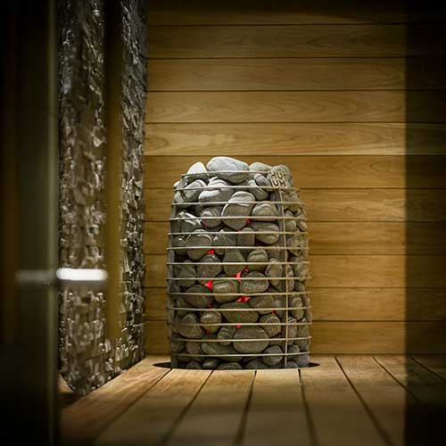 HUUM HIVE Mini electric sauna heater with stacked sauna stones inside wooden sauna room