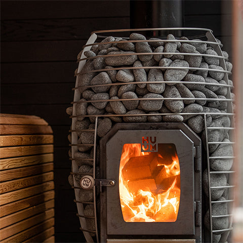 HUUM HIVE Wood 17kW sauna stove with visible flames and sauna stones in a wooden sauna interior