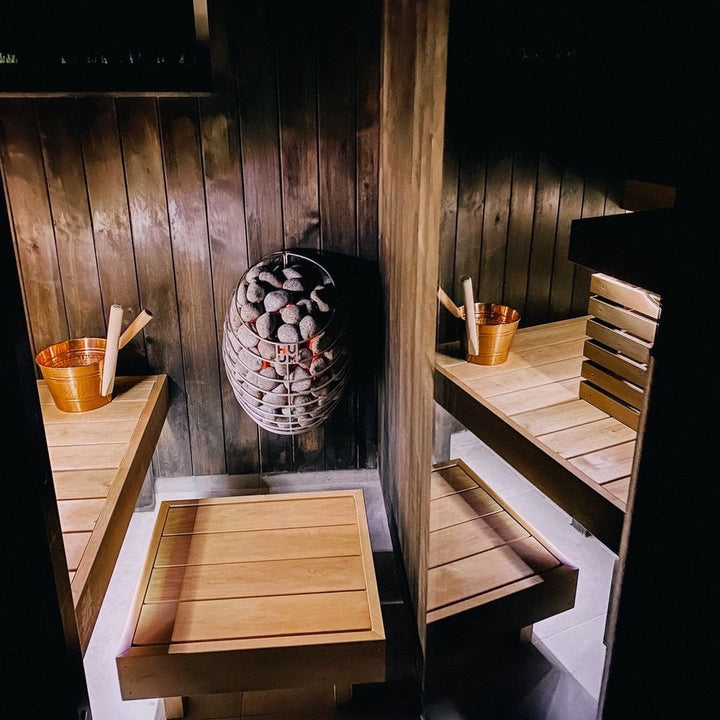 HUUM DROP 6.0kW sauna heater mounted on dark wood wall with sauna stones, benches and wooden buckets
