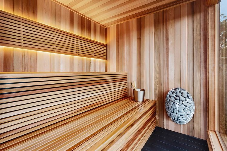 Modern cedar sauna interior with wall mounted HUUM DROP 6.0kW sauna heater filled with stones wooden benches and water bucket