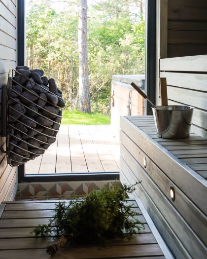 HUUM DROP 7.5kW sauna heater mounted on wall with stone basket bench bucket birch whisk and forest view
