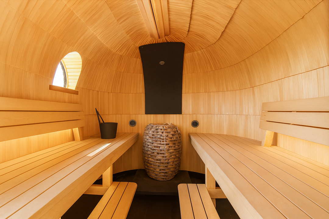 HUUM HIVE Series sauna heater centered in barrel style wooden sauna with benches and ladle bucket