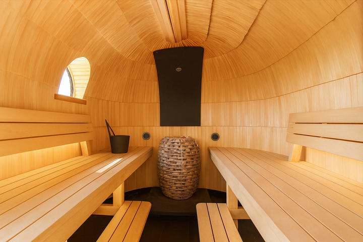 HUUM HIVE Series sauna heater centered in barrel style wooden sauna with benches and ladle bucket