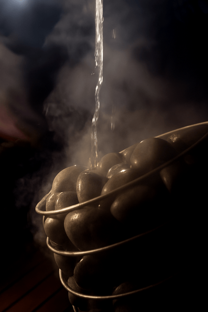 Bucket filled with HUUM sauna heater stones with water pouring over them, creating steam