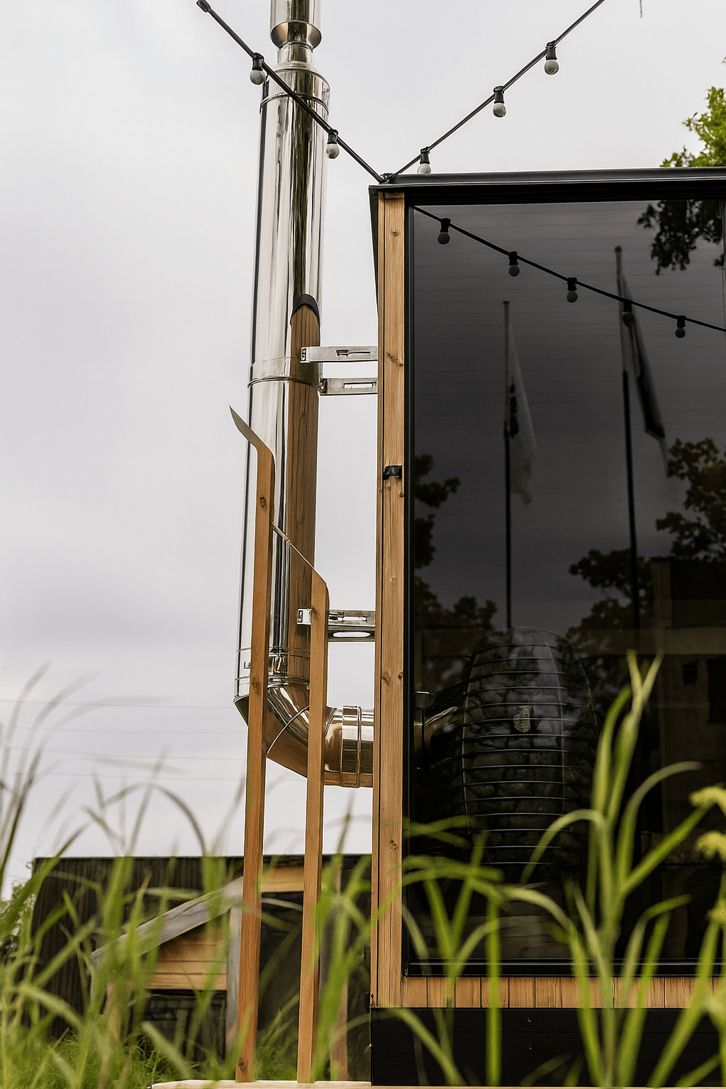 HUUM thru-wall chimney kit installed on a wooden sauna with glass exterior and outdoor lights