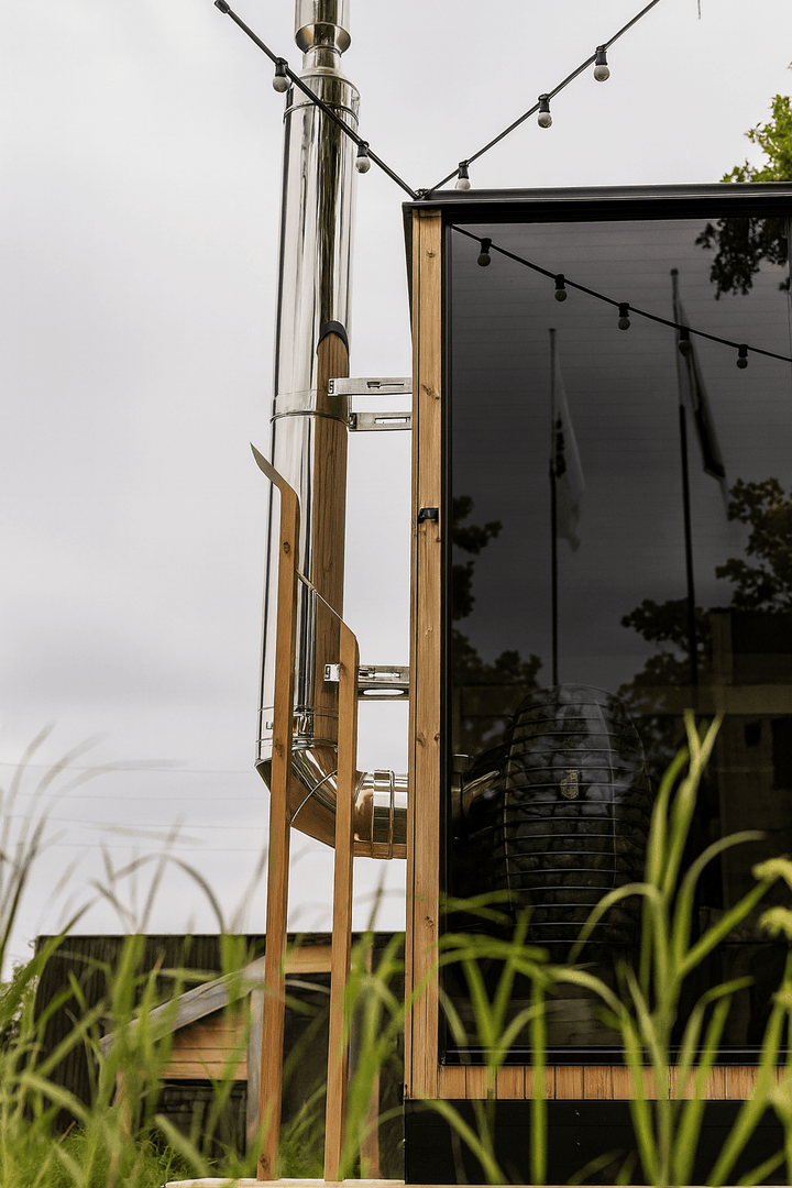 HUUM thru-wall chimney kit installed on a wooden sauna with glass exterior and outdoor lights