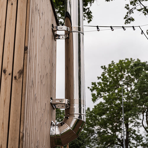 HUUM thru-wall chimney kit stainless steel pipe mounted on wooden exterior wall with outdoor lights