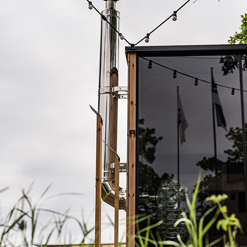 HUUM thru-wall chimney kit stainless steel chimney pipe installed on outdoor wooden sauna with string lights