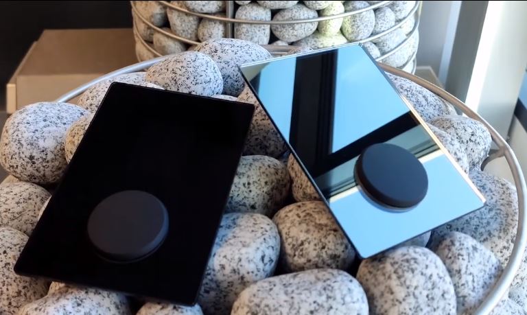 HUUM UKU Mirror sauna control device in black and reflective designs placed on gray sauna stones