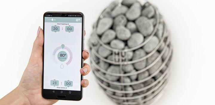 HUUM UKU Wi-Fi sauna controller app displayed on smartphone held next to sauna heater stones