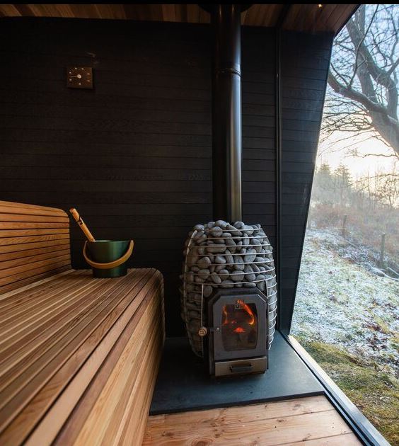 HUUM wood burning sauna stove with stone enclosure inside wooden sauna room near large window