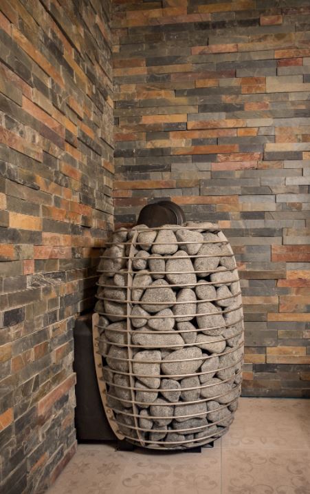 HUUM wood burning sauna stove filled with stones inside a sauna with stone wall