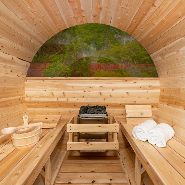 Interior view of a luxury barrel sauna with wooden benches, heater, and rolled white towels