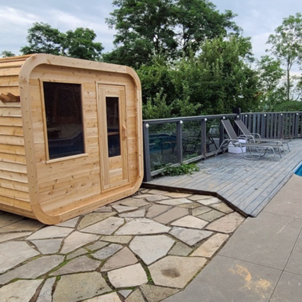 Leisurecraft traditional outdoor luxury sauna made of wood next to poolside deck with lounge chairs