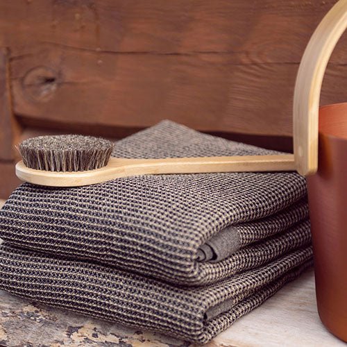 Rento natural bath brush for sauna with soft bristles next to stacked towels