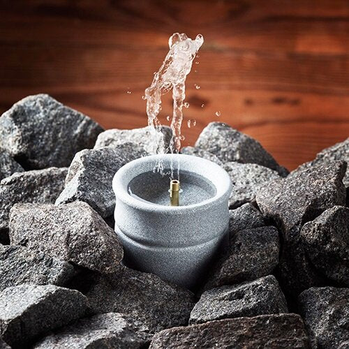 Hukka Finnish soapstone sauna accessory water dispenser nestled among sauna stones creating steam splash