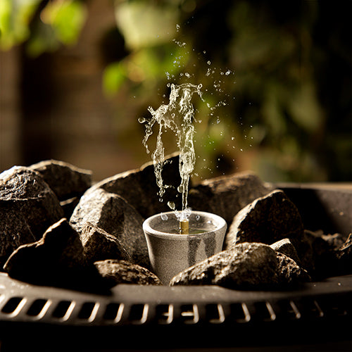 Hukka sauna fountain and diffuser ceramic cup fountain surrounded by hot sauna stones with water splash