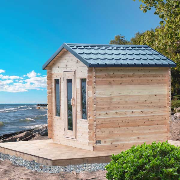 Leisurecraft traditional outdoor wooden sauna with glass door and metal roof on a beach setting