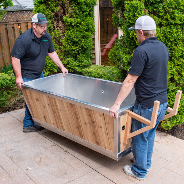 Two men carrying a Leisurecraft Polar Plunge Tub for sale with a wooden and stainless steel design