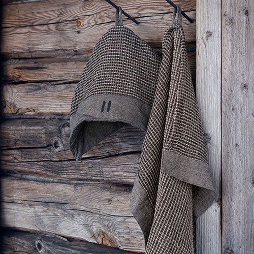 Rento Kenno sauna hat hanging beside a towel against a rustic wooden backdrop