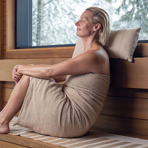 Woman relaxing in a sauna with Rento Kenno sauna pillow for added comfort and support