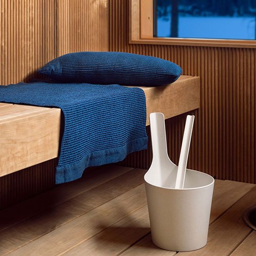 Rento Kenno sauna pillow in blue placed on a wooden sauna bench next to a white bucket