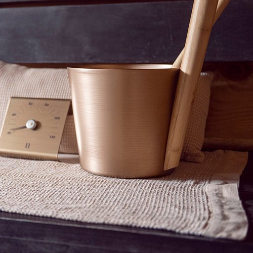 Rento sauna seat cover displayed with a wooden bucket and timer for a complete sauna experience