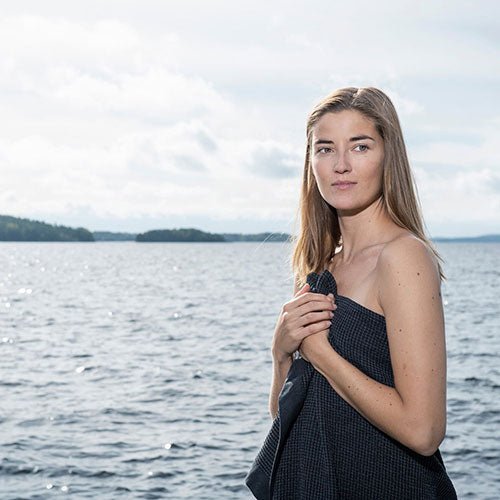Woman holding a Rento Kenno spa towel by the lake, showcasing its elegant design and versatility