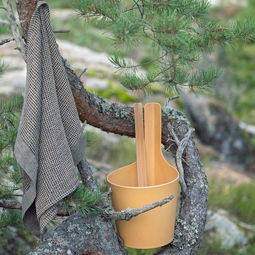 Rento Pisara sauna bucket in orange with wooden ladles hanging on a tree branch outdoors